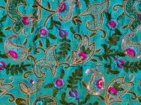 Tissu vert avec motifs floraux brodés colorés.